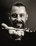 Portrait of Emre, a bearded barber, holding out his scissors