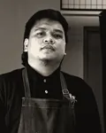 Portrait of Hafiz in a denim apron beside a barber chair