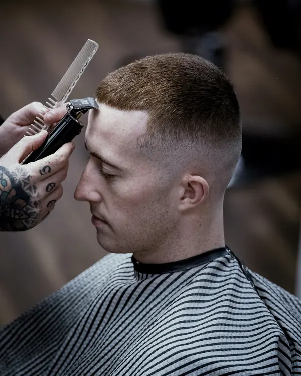 Barber shaping a short crew cut with a high fade