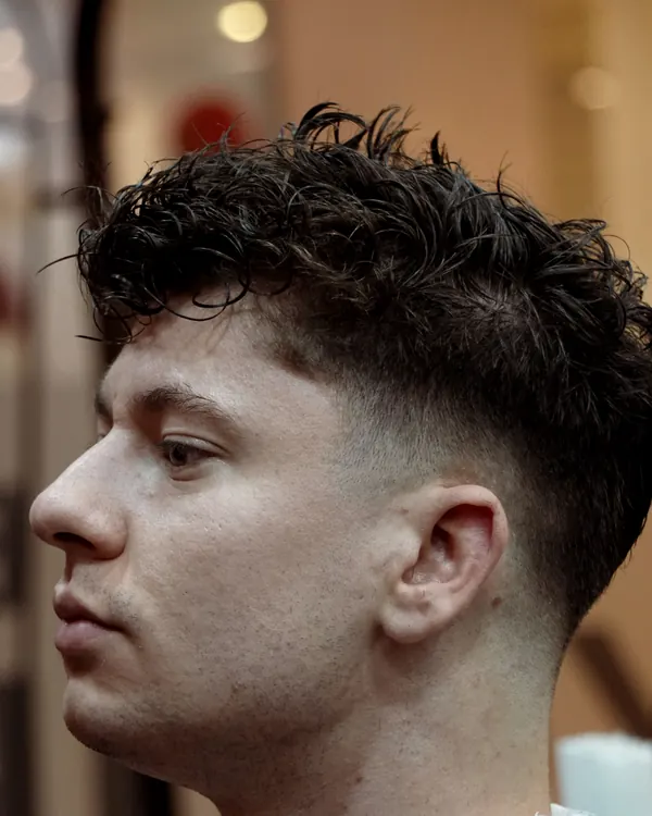 Curly textured crop with a low taper fade, side profile
