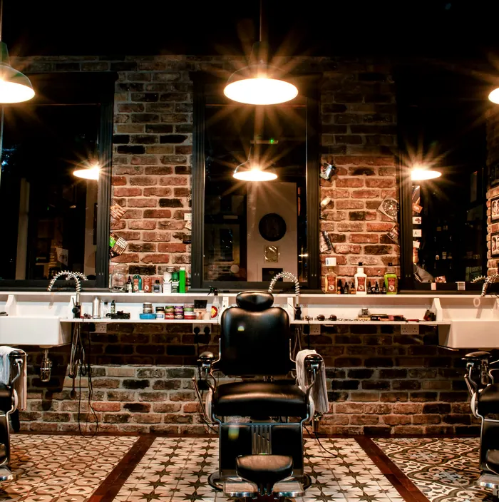 Inside the shop: barber chairs under warm pendant lights, brick walls and patterned floor tiles