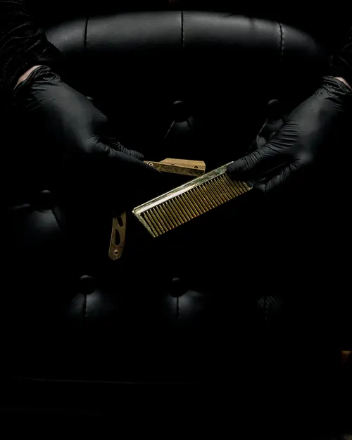 Barber in black gloves holding a brass comb in front of a leather chair